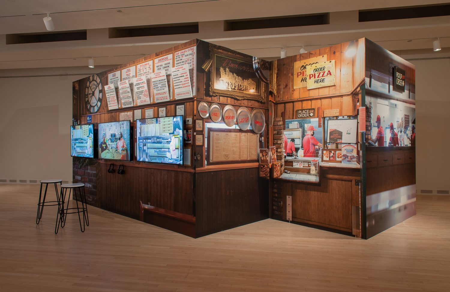 Mario Ybarra Jr., “Personal, Small, Medium, Large, Family,” 2021, custom stage facade with videos, photographic wallpaper, framed photographs, 3 aluminum pizza pans, hand-painted canvas signs, wood. On view in “Undoing Time: Art and Histories of Incarcera